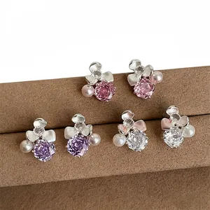 Close-up of floral stud earrings with colored zircons and pearls on brown stand