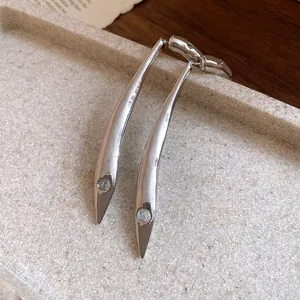 Detailed macro view of long curved silver drop earrings featuring a minimalist geometric design