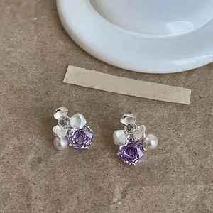 Macro view of delicate floral stud earrings featuring purple zirconia and elegant pearls.