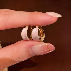 Dettaglio di orecchini a cerchio placcati oro 18k con smalto rosa tra le dita
