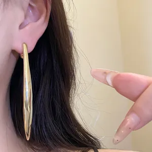 Close-up detail of a long metallic golden water-drop pendant earring on an ear
