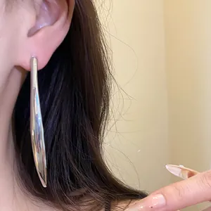 Close-up view of a minimalist silver metallic long drop earring worn on a model's ear