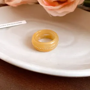 Close-up of an elegant yellow resin ring with a gold bead chain detail on a white plate