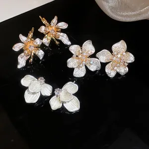 Close-up view of three French style zircon and white enamel flower earrings on black surface