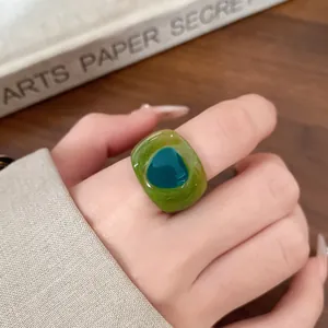Detailed view of a chunky green resin ring with a marbled texture and blue circular inlay.