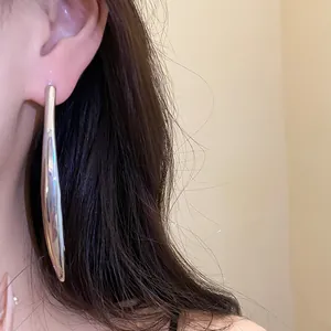 Close-up detail view of elegant long curved silver metal pendant earring worn on ear