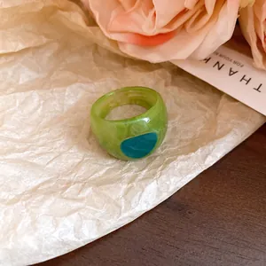 Detailed view of a green resin tie-dye ring featuring a teal oval inlay on artistic background
