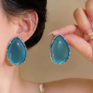 Large teal teardrop resin earrings with textured silver bezel on model's ear