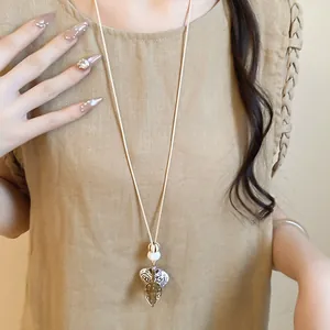 Lange Kette im Ethno-Stil mit Harzanhänger auf einem beigefarbenen Leinenkleid.