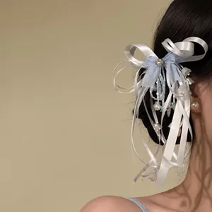 Detail view of a light blue and white ribbon bow hair clip with bead fringe on a model.