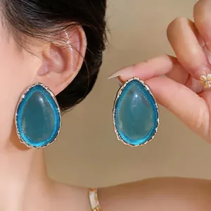 Macro view of oversized teardrop earrings featuring teal resin and polished silver trim