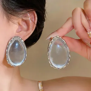 Detail view of oversized clear resin teardrop earrings with silver textured trim.
