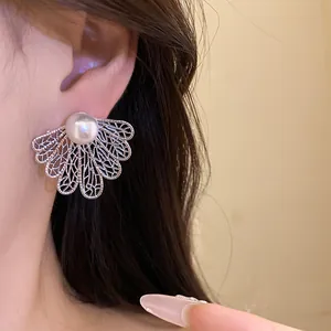Close-up detail of retro silver needle hollow leaf earrings with white pearls worn on ear.