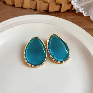 Close-up detail of elegant teal teardrop resin earrings with gold wavy textured edge