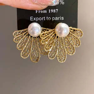 Close-up of vintage gold leaf earrings with white pearls and hollow pattern detail.