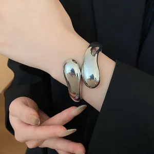 Vista detallada de un brazalete de plata minimalista con forma de gota retorcida en una muñeca.