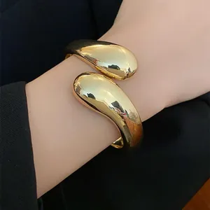 Detalle de un brazalete de gota dorado minimalista con un acabado metálico pulido