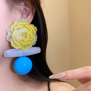 Close-up view of oversized resin flower earrings with blue sphere and marbled bar