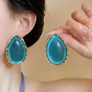 Detailed view of oversized teal resin teardrop earrings with gold-toned trim.