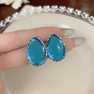 Macro detail of blue teardrop resin earrings with textured silver-toned borders