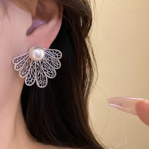 Close-up of elegant vintage pearl stud earring with silver leaf filigree worn on ear.