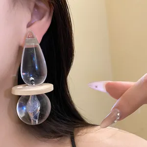 Close-up detail view of a large transparent resin drop pendant earring worn on ear