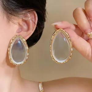 Close-up view of oversized teardrop resin earrings featuring textured gold-tone frames