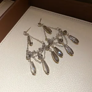 Détail de boucles d'oreilles argentées à pompons avec pierres grises en forme de goutte