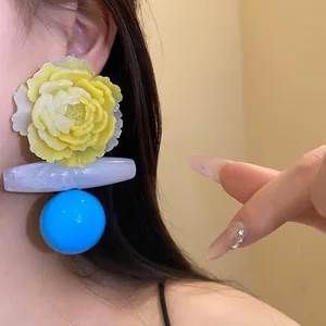 Close-up of oversized yellow resin flower earrings featuring a blue spherical pendant