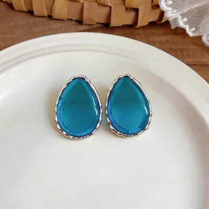 Close-up of teardrop resin earrings with silver wavy edge on a white ceramic plate