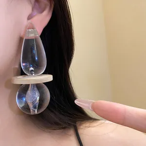 Close-up of exaggerated clear resin drop earring with wooden disc detail on ear.