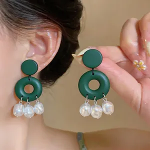 Close-up of elegant dark green geometric drop earrings with white baroque pearl charms.