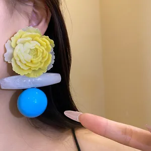 Close-up detail of retro exaggerated resin flower dangle earrings with blue sphere