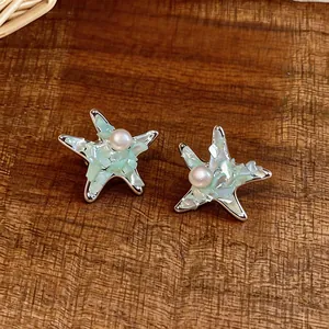 Macro view of elegant star-shaped stud earrings featuring mint green stones and central pearl