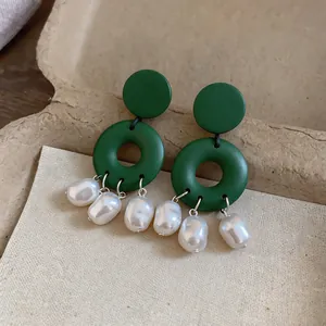 Macro detail of dark green geometric earrings with dangling baroque pearls on textured card