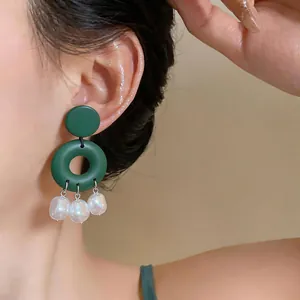 Close-up of geometric dark green earrings with hanging baroque pearl charms on a model