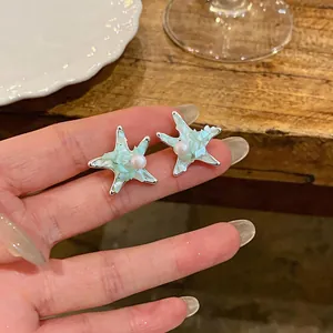 Detailed macro view of starfish stud earrings with white pearls and mint green shell inlay