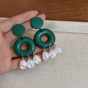 Close-up detail of green geometric hoop earrings with baroque pearl dangles held in hand