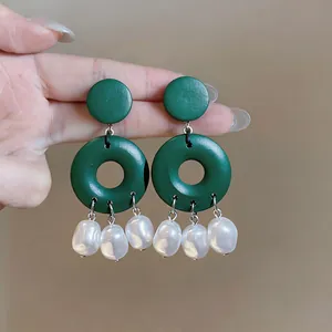 Close-up detail showing green geometric dangle earrings with white irregular pearl pendants
