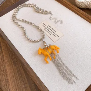 Close-up of a stylish orange resin horse pendant necklace featuring silver chain tassels
