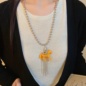 Close-up of vibrant orange resin pony pendant necklace with silver chain tassels