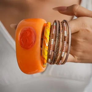 Close-up of vibrant orange resin bangle and multi-layer leather bracelets stack