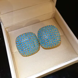 Close-up of vintage square stud earrings featuring turquoise pave stones in gold lattice