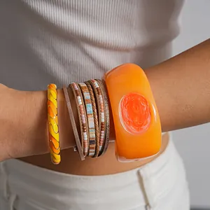 Detailed view of bohemian layered leather and orange resin bracelets worn on wrist