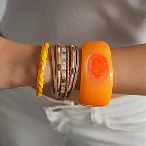 Close-up of stacked bohemian bracelets featuring leather, beads, and orange resin bangles