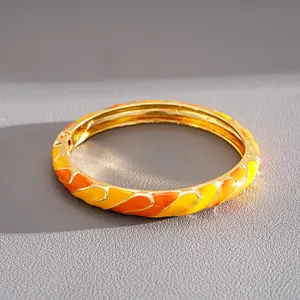 Detail view of a gold-toned bangle featuring vibrant yellow and orange enamel patterns.