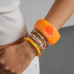 Detailed view of layered bohemian bracelets with orange resin bangle and leather wrap