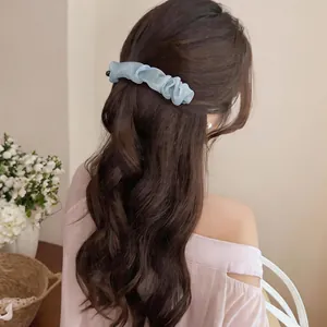 Back view of a woman wearing a light blue ruffled mesh hair clip on wavy brown hair