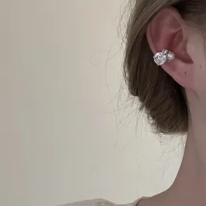 Nahaufnahme eines eleganten minimalistischen Ohrmanschetten mit Zirkon und Perle am Ohr getragen