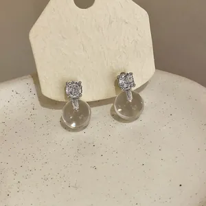 Dettaglio di orecchini a lobo in argento minimalisti con zircone e goccia sferica.